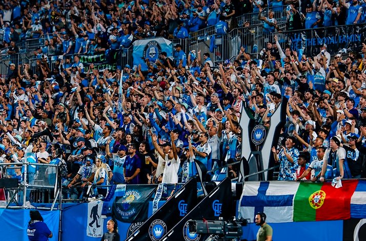 Closeup of fans, some holding large banners and crests for Charlotte Football Club