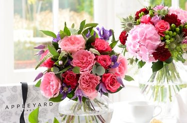 A pair of flower bouquets in vases, displayed alongside a package branded with the Appleyard Flowers logo. Mastercard logo is in bottom right corner.