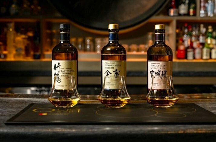 Three bottles of Nikka Japanese whiskey and tasting glasses lined up on a branded Quin Bar placemat.