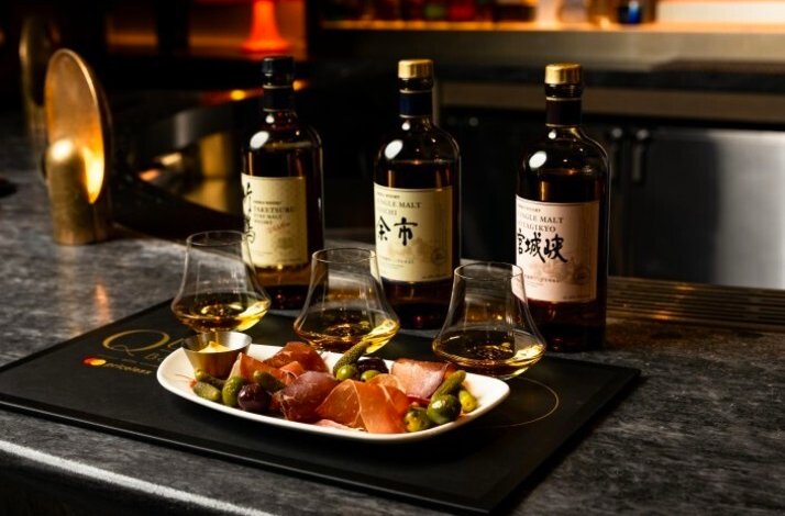 Japanese whiskey flight with three bottles and glasses served alongside a charcuterie plate with olives.