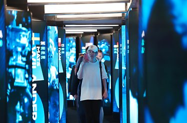 A visitor taking a video while walking down a hallway with glowing vertical screens of tennis player names.