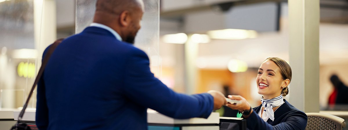 Airport staff member assisting a traveller at a Fast Track lane counter, exchanging travel documents.