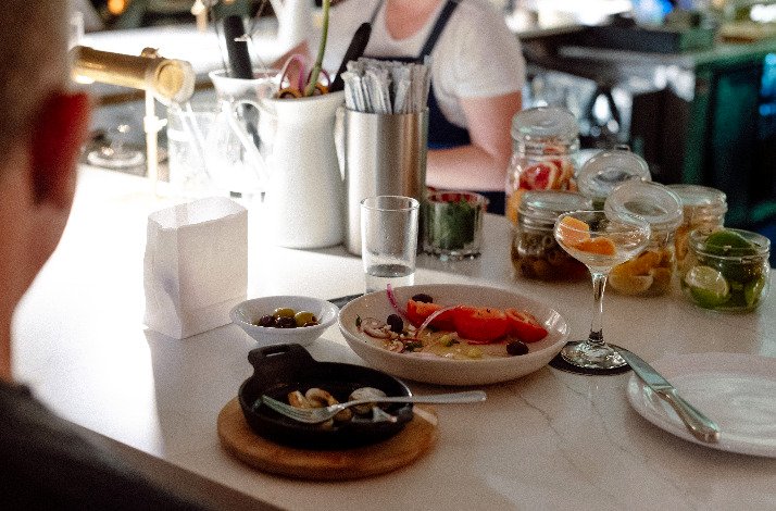 An elegant dining setup with dishes including olives, fresh vegetables, and drinks, alongside bar accessories
