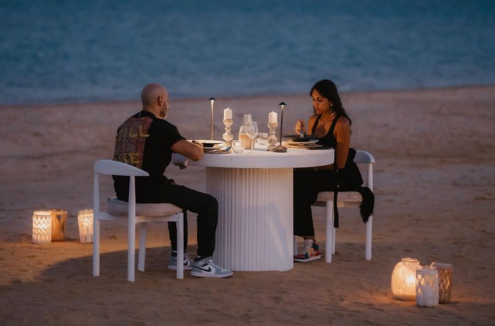 A couple at the beach enjoying a meal on a dimly lit table.