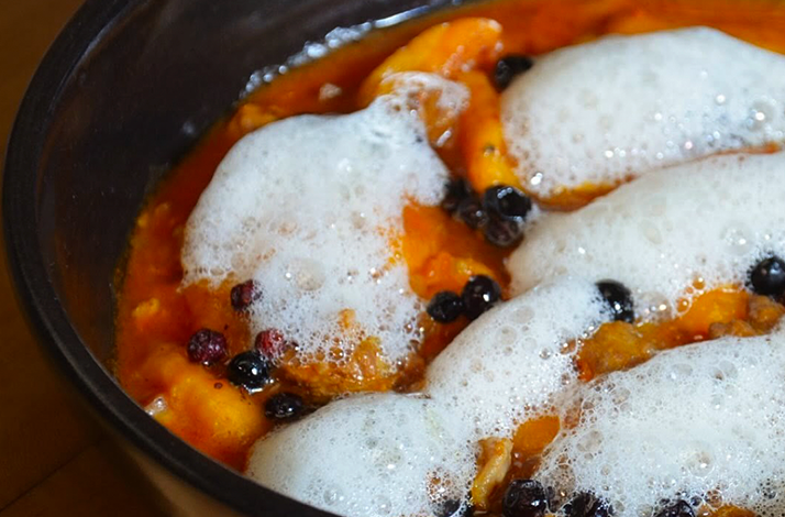 A vibrant dish featuring rich orange tones, light foam, and small berries that highlight the experience's innovative culinary approach.