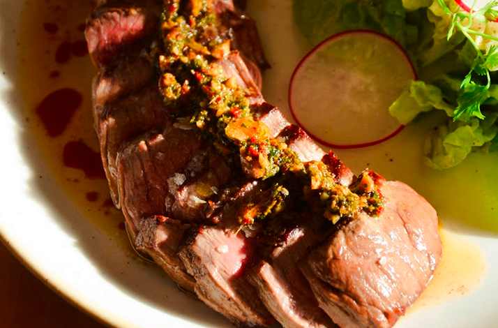 A juicy cut of meat served with a flavorful herb and spice topping, accompanied by fresh vegetables