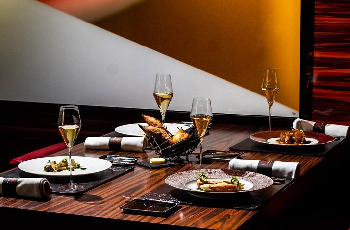 Elegant dining table set with champagne flutes and plated courses in a warm, modern dining room at L’Atelier Miami.