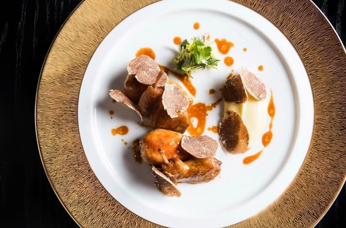 Fine-dining plate with roasted meat, shaved truffles, and sauce accents arranged in a minimalist presentation.