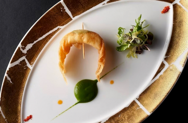 Delicate shrimp appetizer on an oval plate with green purée and microgreens, styled with clean, modern plating.