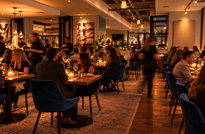 Porto Boston's candlelit dining room filled with guests at wooden tables with blue velvet chairs during a busy evening service.