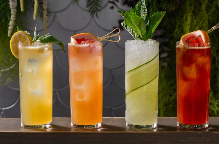 Four garnished cocktails in tall glasses — citrus, grapefruit, cucumber-mint, and berry — lined up at Porto Boston's bar.