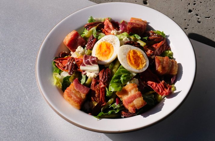 Salad plate with egg halves, bacon pieces, pecans, and greens in bright sunlight.